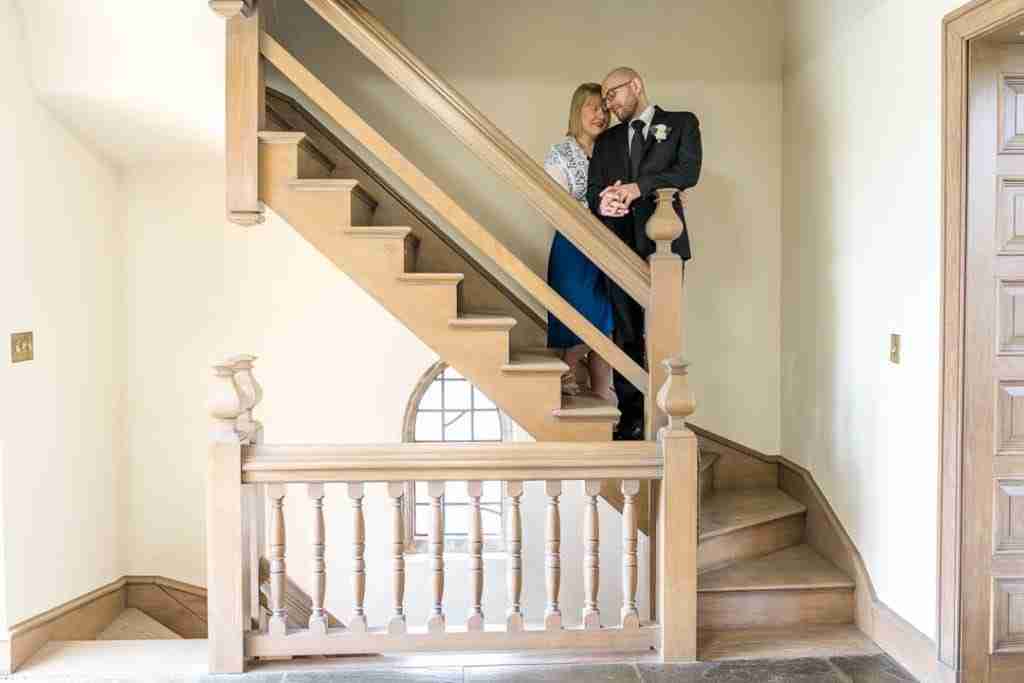 A couple embracing on a wooden staircase in a well-lit room.