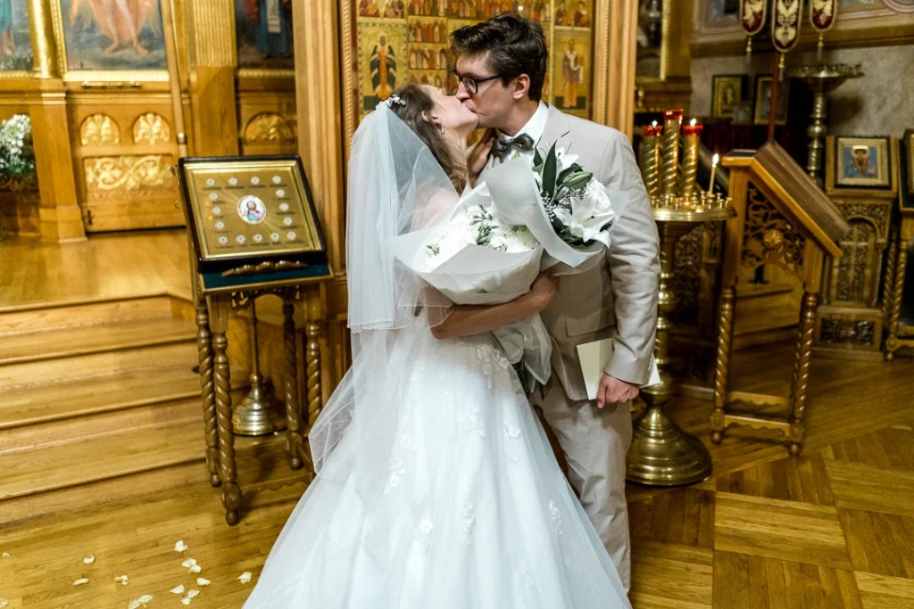 Bride and groom, kissing while holding flowers