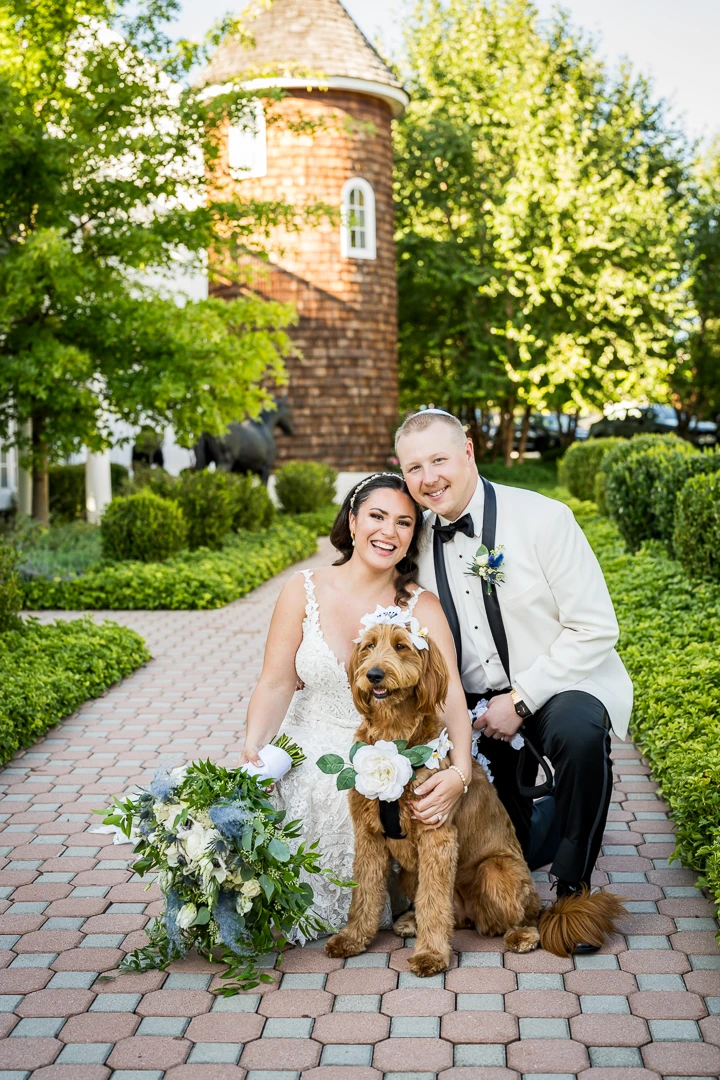 Bride and groom smiling with their dog on wedding day at outdoor garden venue