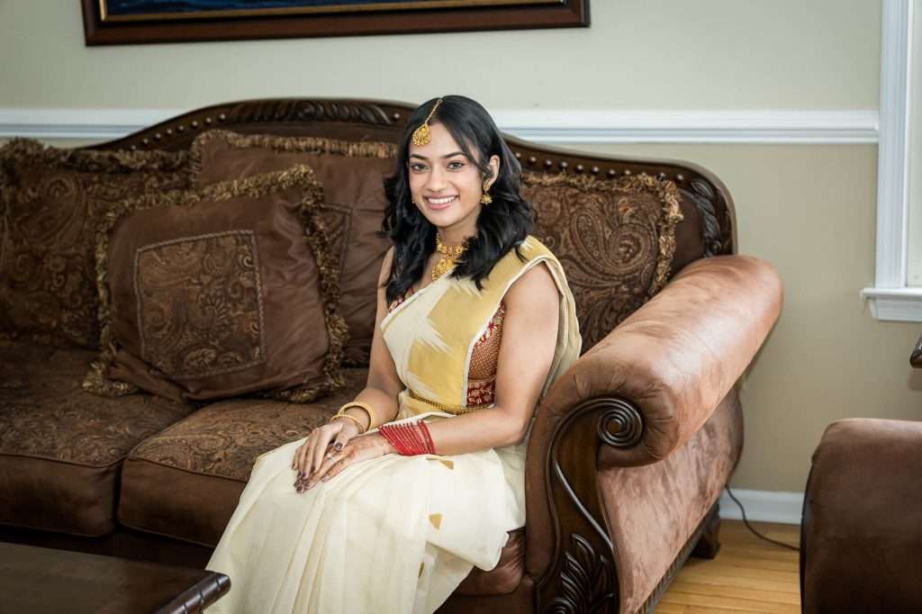 Serene Beauty: A radiant bride in a golden saree sits gracefully on an ornate sofa, her joy evident in her bright smile.