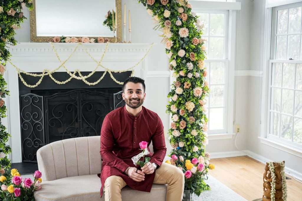 Gentle Moments: The groom seated casually, holding a single rose, surrounded by a beautifully floral-adorned setting, representing anticipation and love.