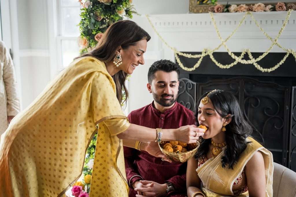 Feeding Ceremony Moment: An intimate ceremony moment as a loved one feeds the bride-to-be, symbolizing affection and family bonds in this beautifully captured Indian engagement tradition.