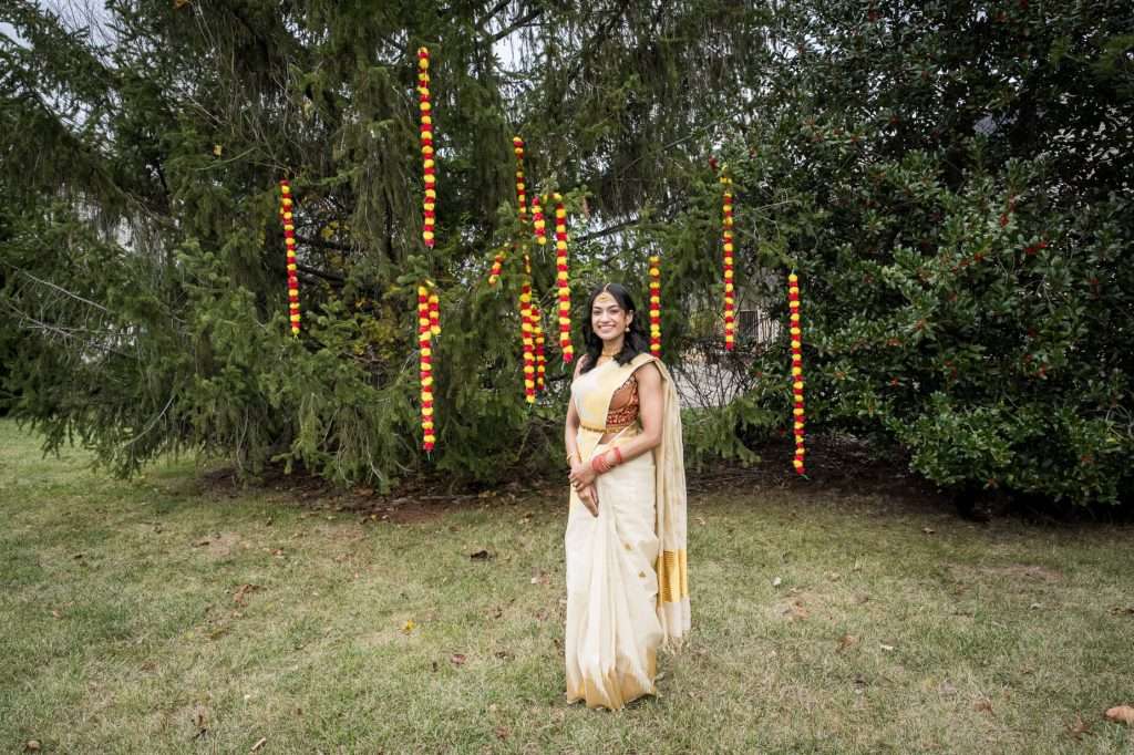 Celebrate the beauty of tradition and nature with this stunning portrait of a bride in traditional attire, set against the serene backdrop of lush greenery adorned with festive lights.