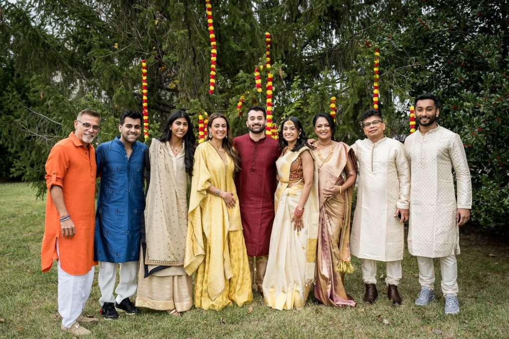 A joyful family gathering outdoors under whimsical floral hangings, showcasing the rich cultural heritage and close-knit bonds during a special engagement celebration.