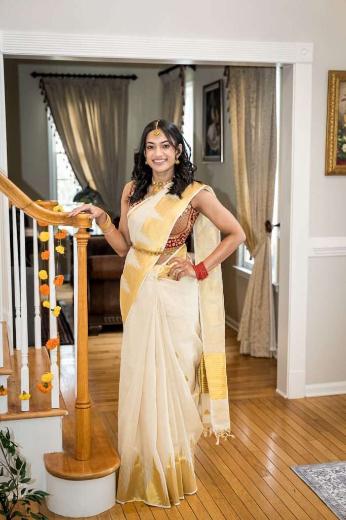 Charming Grace: A charming smile lights up the bride’s face as she poses by the staircase, her saree elegantly draped.