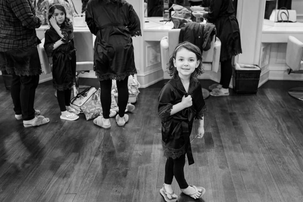 A young flower girl in a black robe smiles at the camera while getting ready for the wedding at The Park Savoy Estate.