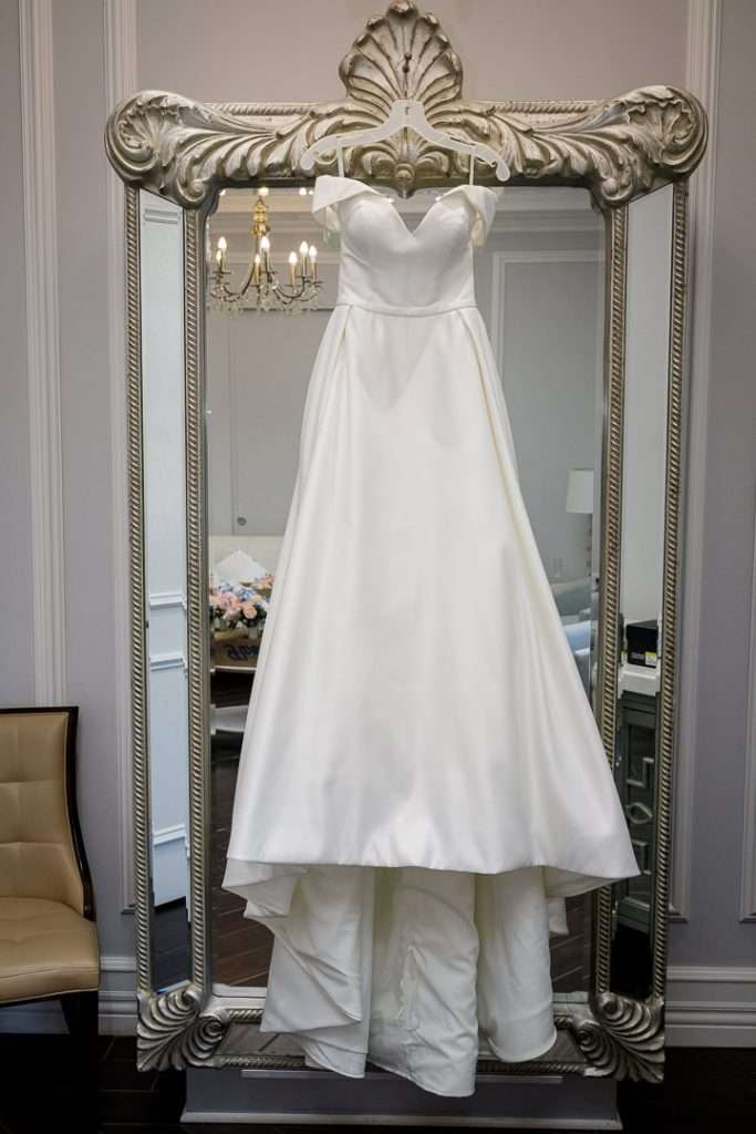 A stunning white wedding dress hangs on an ornate mirror in the bridal suite at The Rockleigh