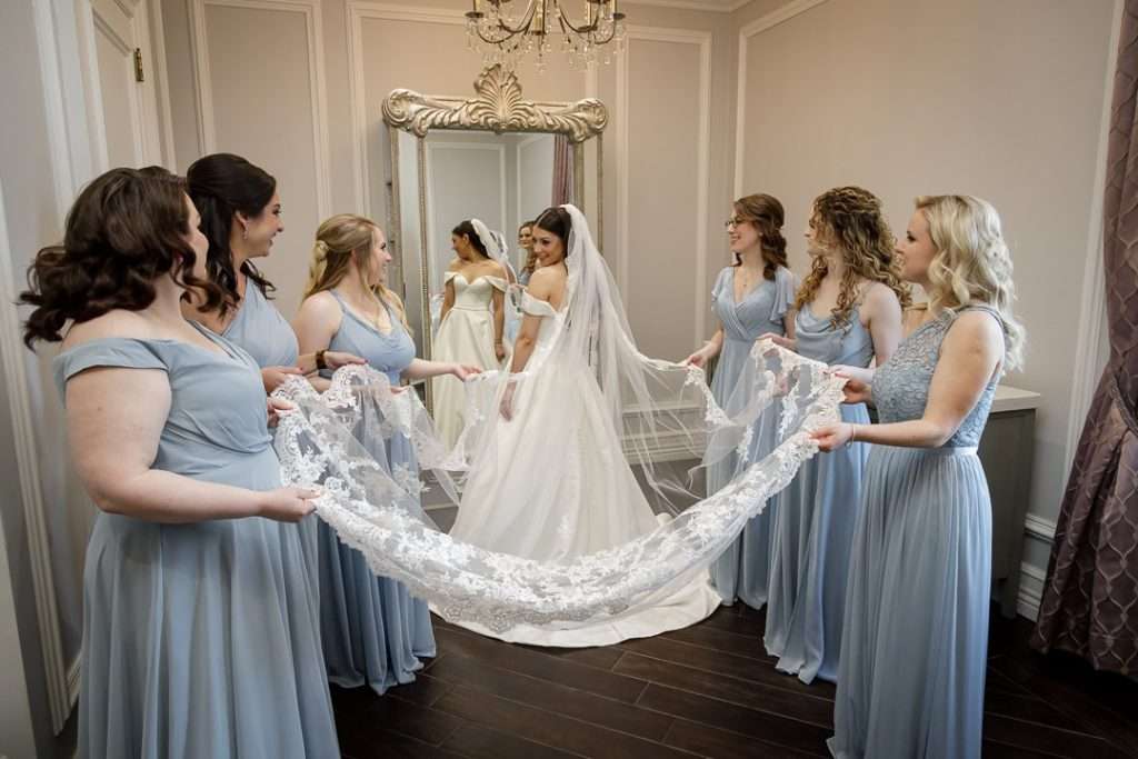  Bridesmaids elegantly hold the bride’s lace veil, creating a picture-perfect moment at The Rockleigh