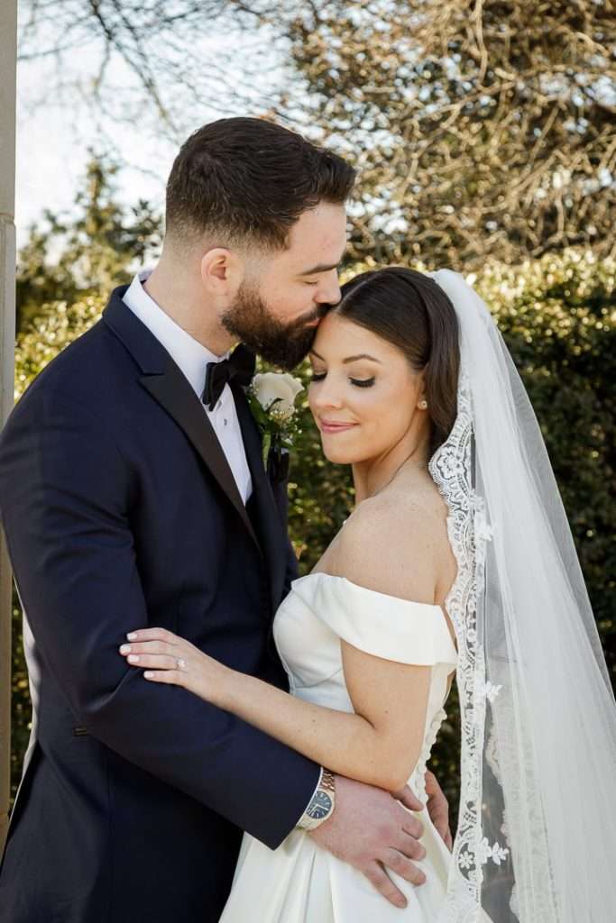 A heartfelt moment as the groom gently kisses the bride’s forehead in The Rockleigh’s garden