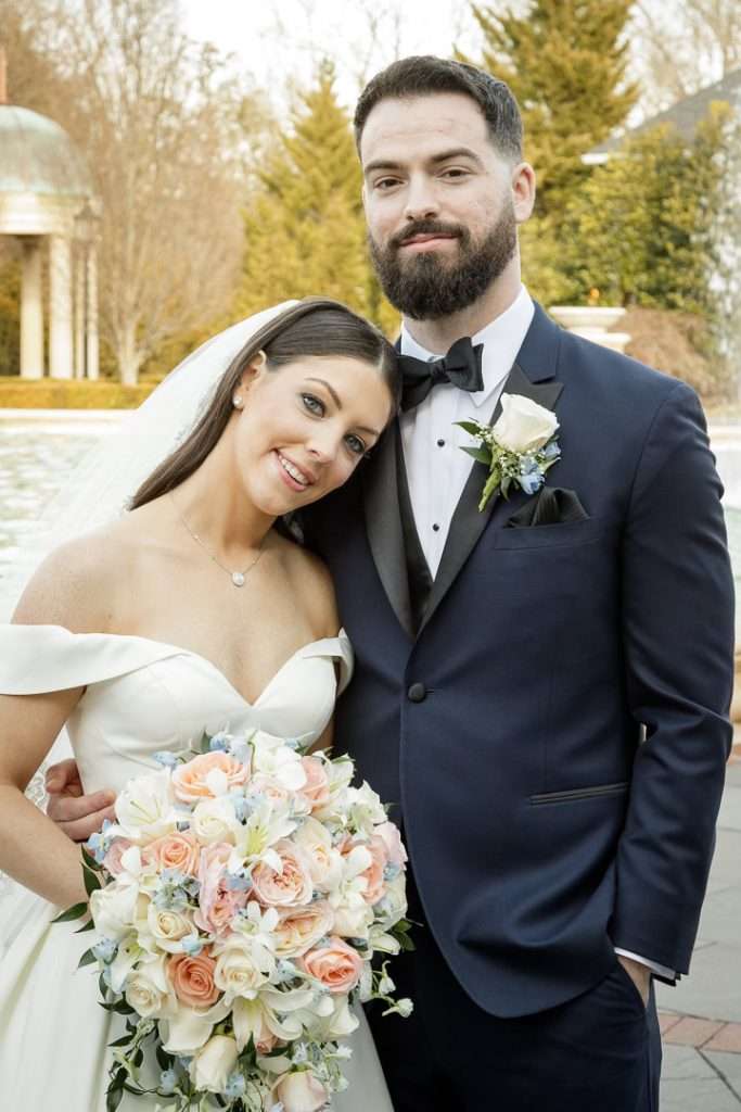 The bride leans on the groom’s shoulder, holding her exquisite bouquet in The Rockleigh’s picturesque setting.