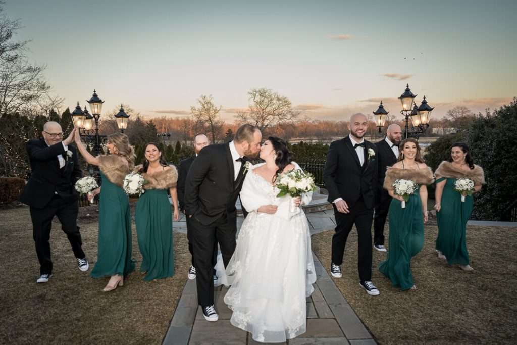 A newlywed couple walks joyfully with their wedding party at The Park Savoy Estate, sharing a kiss as bridesmaids and groomsmen celebrate around them.