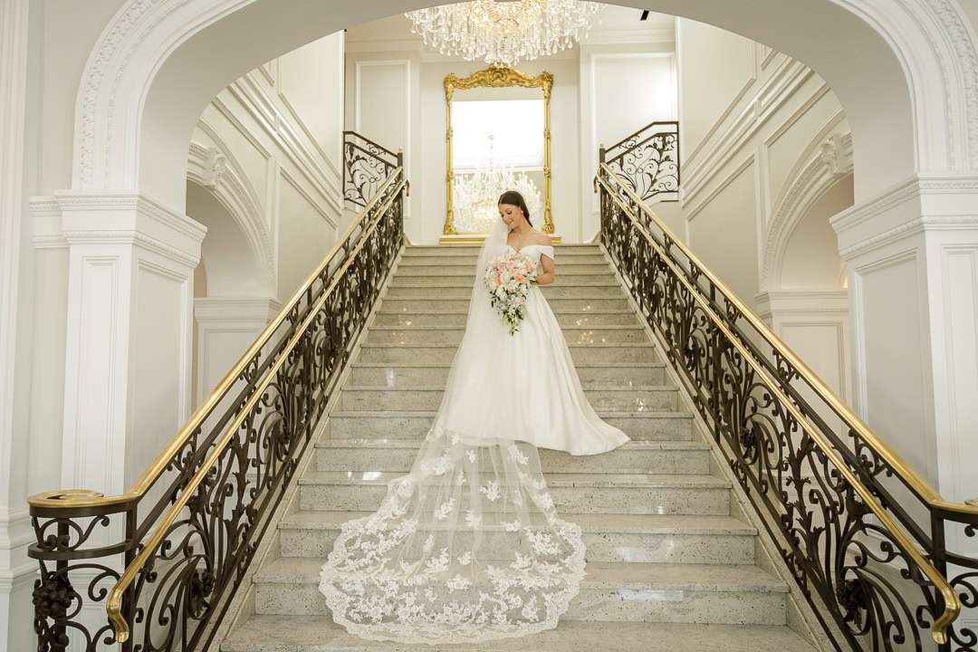 A close-up of the bride smiling, holding her bouquet with a sparkling chandelier in the background at The Rockleigh