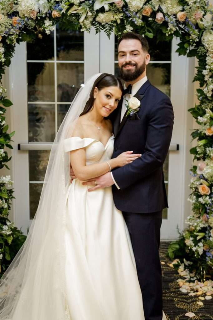 The newlyweds embrace under a floral ceremony arch with glowing candlelight at The Rockleigh