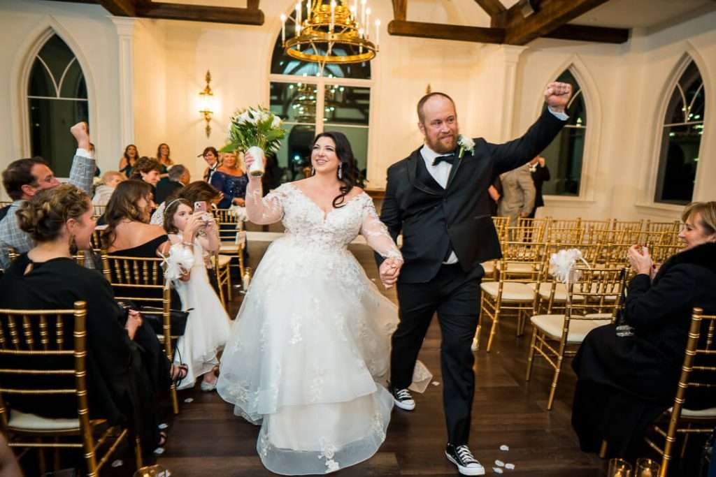 A newlywed couple walks hand in hand down the aisle at The Park Savoy Estate, smiling and celebrating their marriage with family and friends.