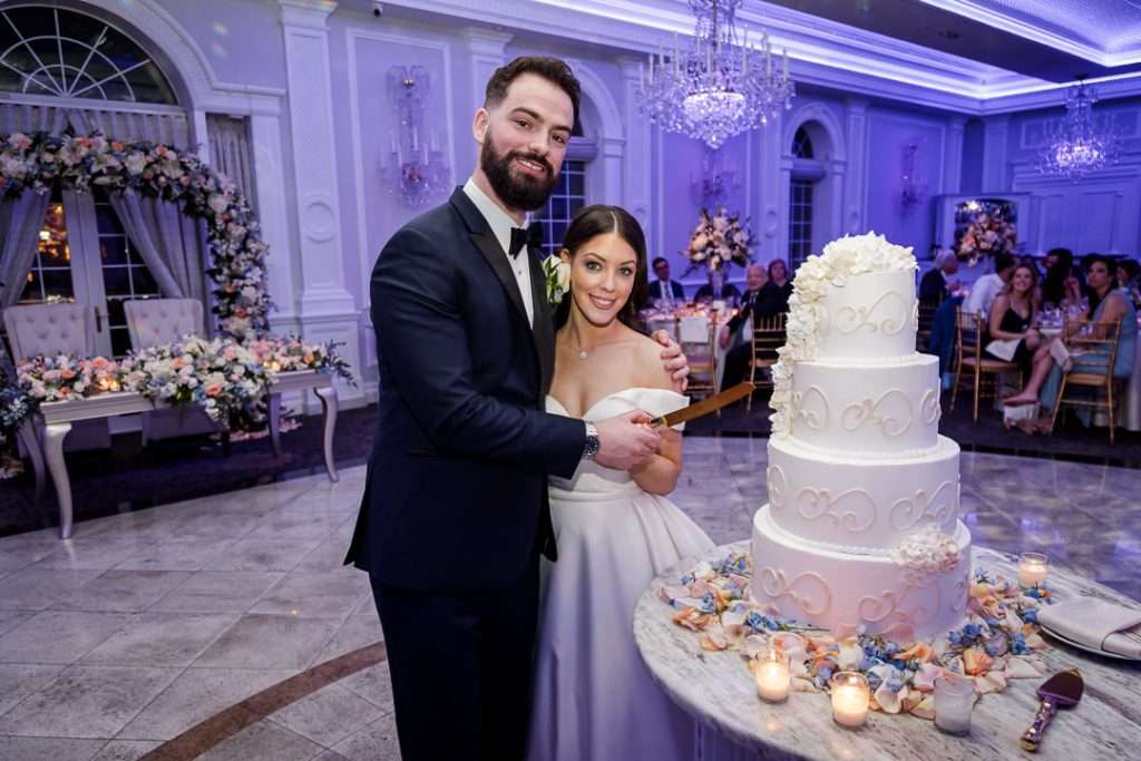 The bride and groom cut into a beautifully decorated tiered wedding cake at their reception in The Rockleigh
