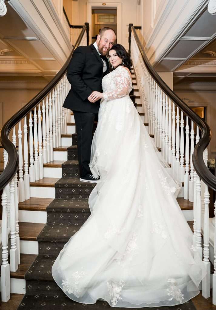 A bride and groom pose together on the grand staircase at The Park Savoy Estate, with the bride's gown cascading down the steps.