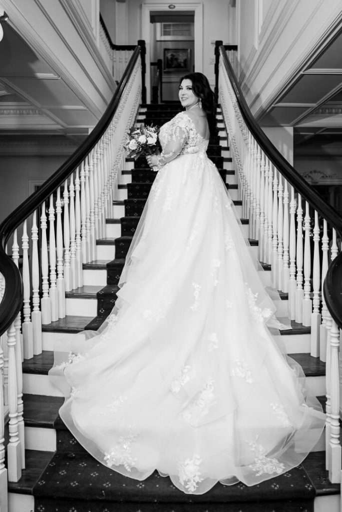 A bride stands gracefully on the grand staircase at The Park Savoy Estate, looking back over her shoulder with an elegant pose.