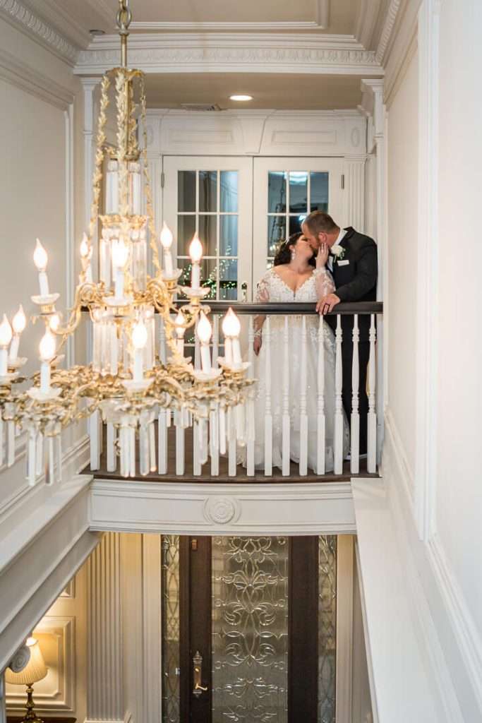 Bride and groom share a romantic kiss on the elegant balcony of The Park Savoy, with a stunning chandelier illuminating the scene.