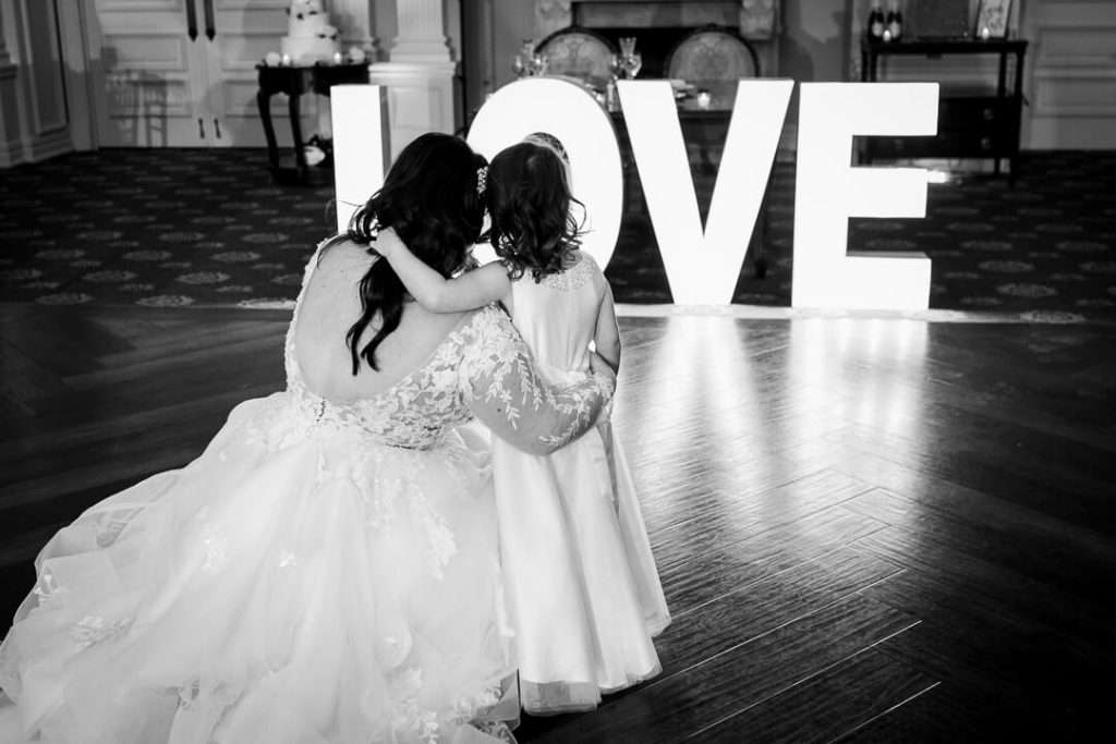 Bride and flower girl share a sweet moment on the dance floor of The Park Savoy, with a glowing "LOVE" sign in the background.