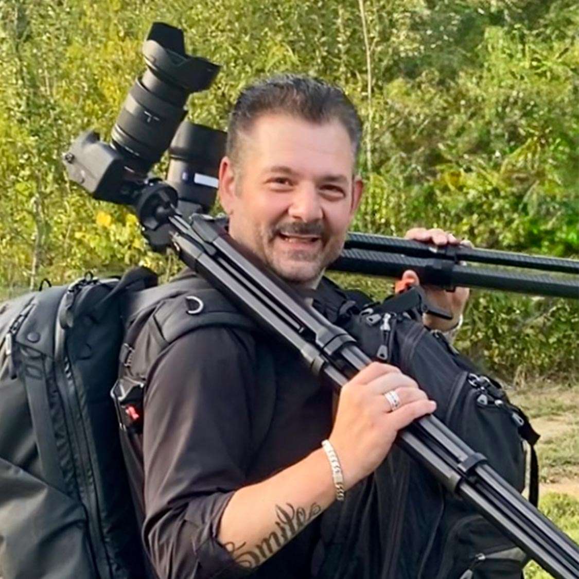 Photographer carrying a tripod with a camera attached with a long lens. Camera bag rucksack on his back. Photographer is Alex Kaplan, New York