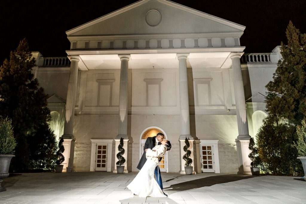 Dramatic nighttime wedding dip at The Palace at Somerset Park – The groom romantically dips his bride in front of the grand entrance of The Palace at Somerset Park, beautifully illuminated at night.