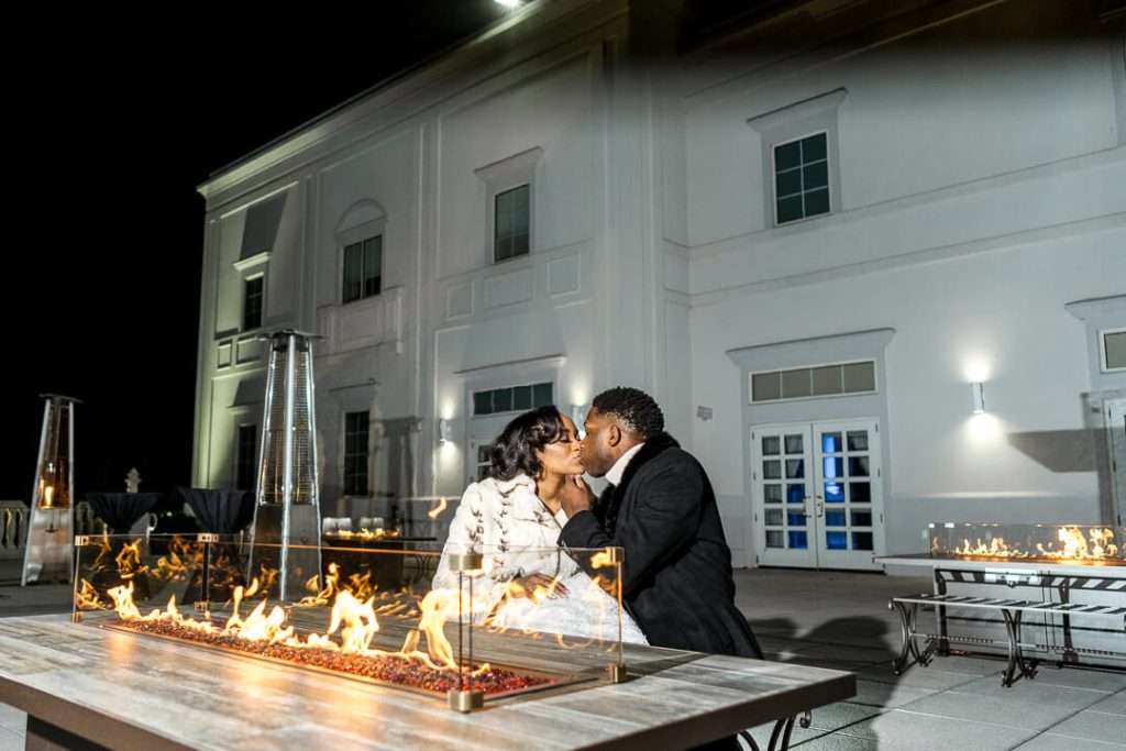 Romantic firepit kiss at The Palace at Somerset Park – The newlyweds share an intimate moment by the firepit on the outdoor terrace of The Palace at Somerset Park, adding warmth to their winter wedding.