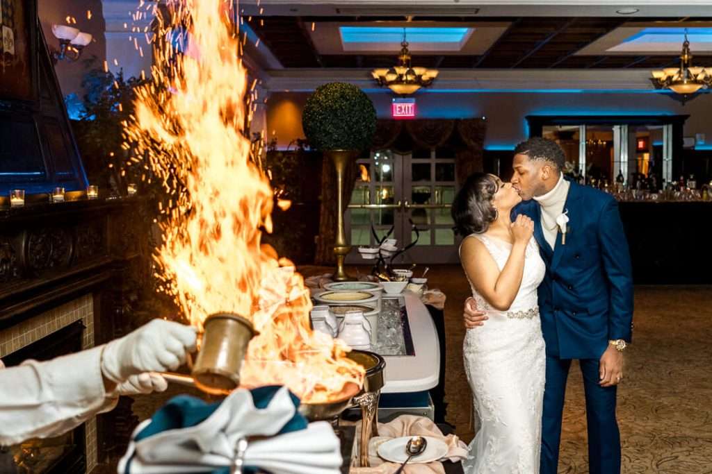 Flaming dessert station with newlywed kiss at The Palace at Somerset Park – A striking shot of the couple kissing while a dramatic flame lights up the dessert station, capturing a unique and unforgettable wedding moment.