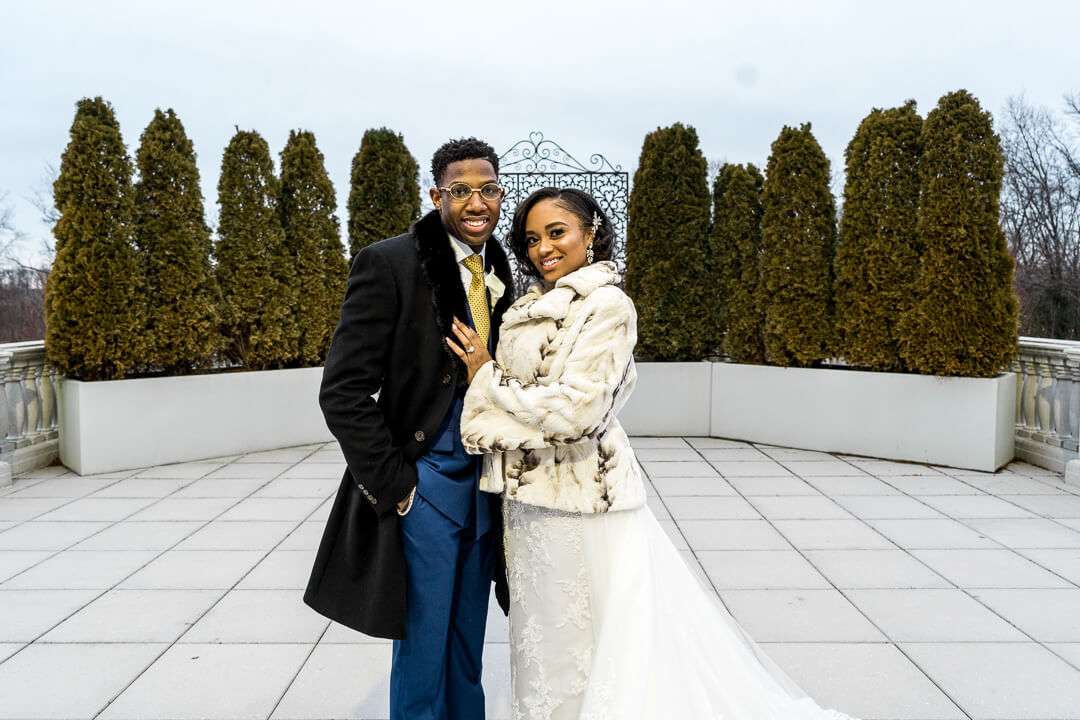 Happy couple posing at The Palace at Somerset Park – The newlyweds share a joyful moment, dressed in winter wedding attire, in front of the venue’s lush greenery.