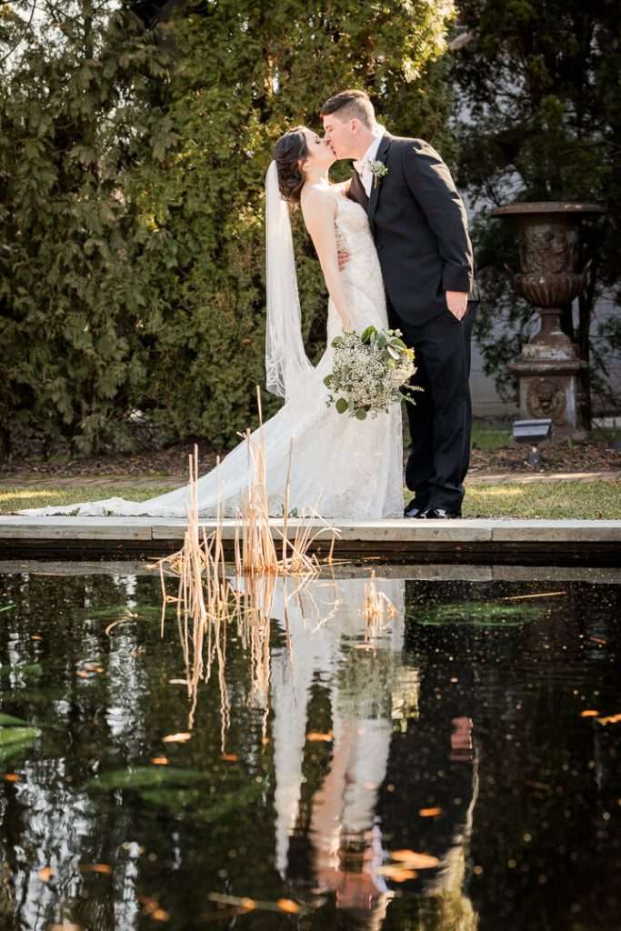 Bride and groom share a romantic kiss by the reflecting pond at Park Savoy