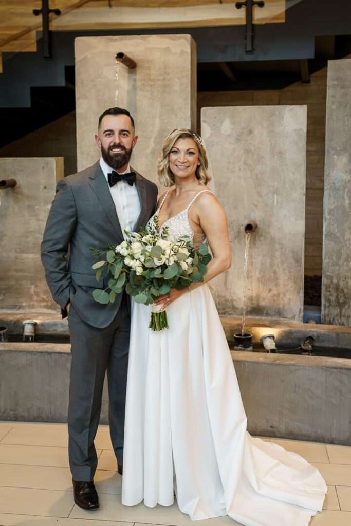 Bride and groom standing together in front of a modern water feature at Stone House at Stirling Ridge.