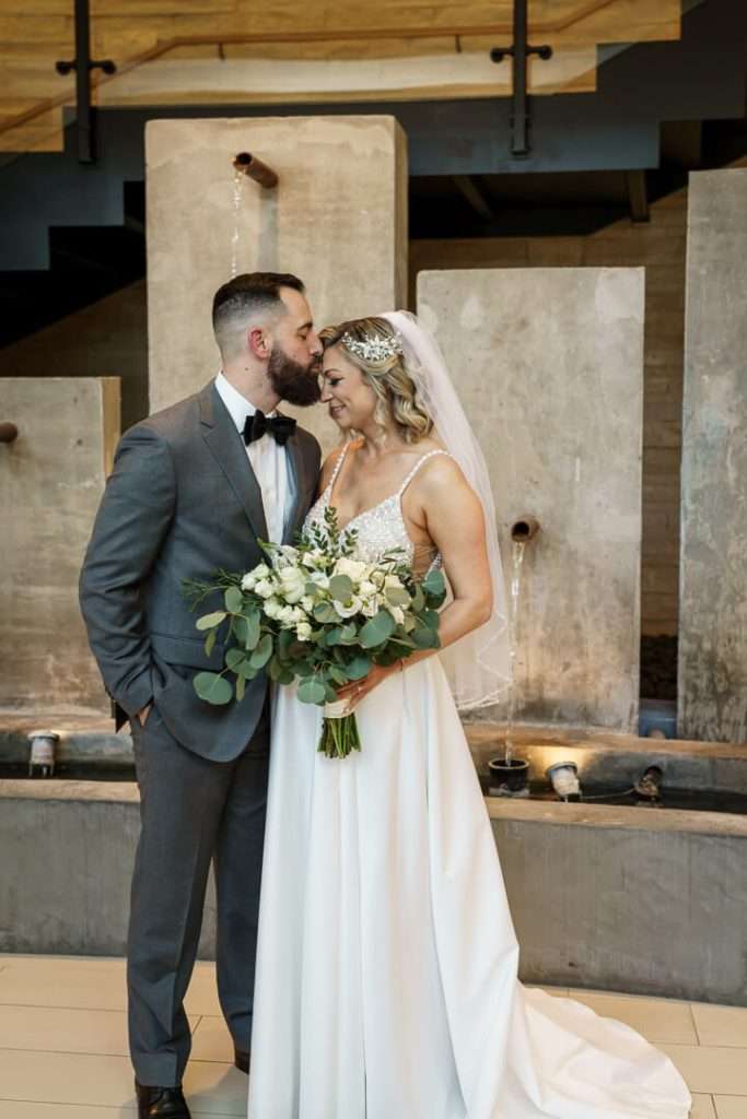 Bride and groom share a romantic moment, touching foreheads in front of a cascading water backdrop at Stone House at Stirling Ridge