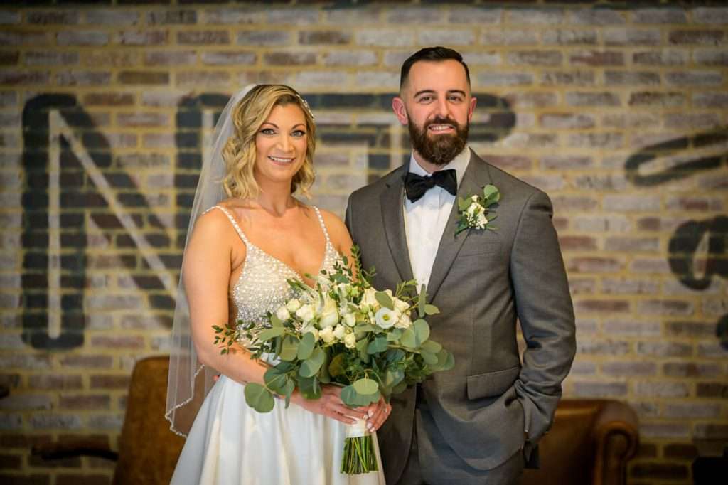 Bride and groom smiling together, dressed elegantly in front of a rustic lounge area at Stone House at Stirling Ridge