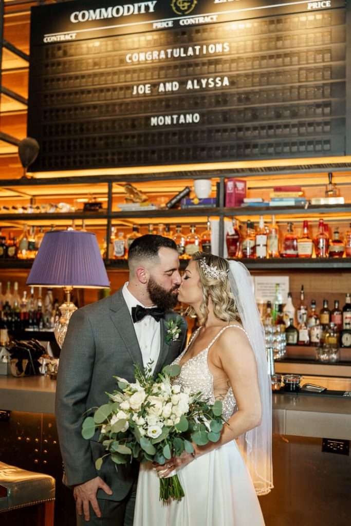 Bride and groom sharing a kiss at the bar, with a "Congratulations Joe and Alyssa" sign in the background at Stone House at Stirling Ridge