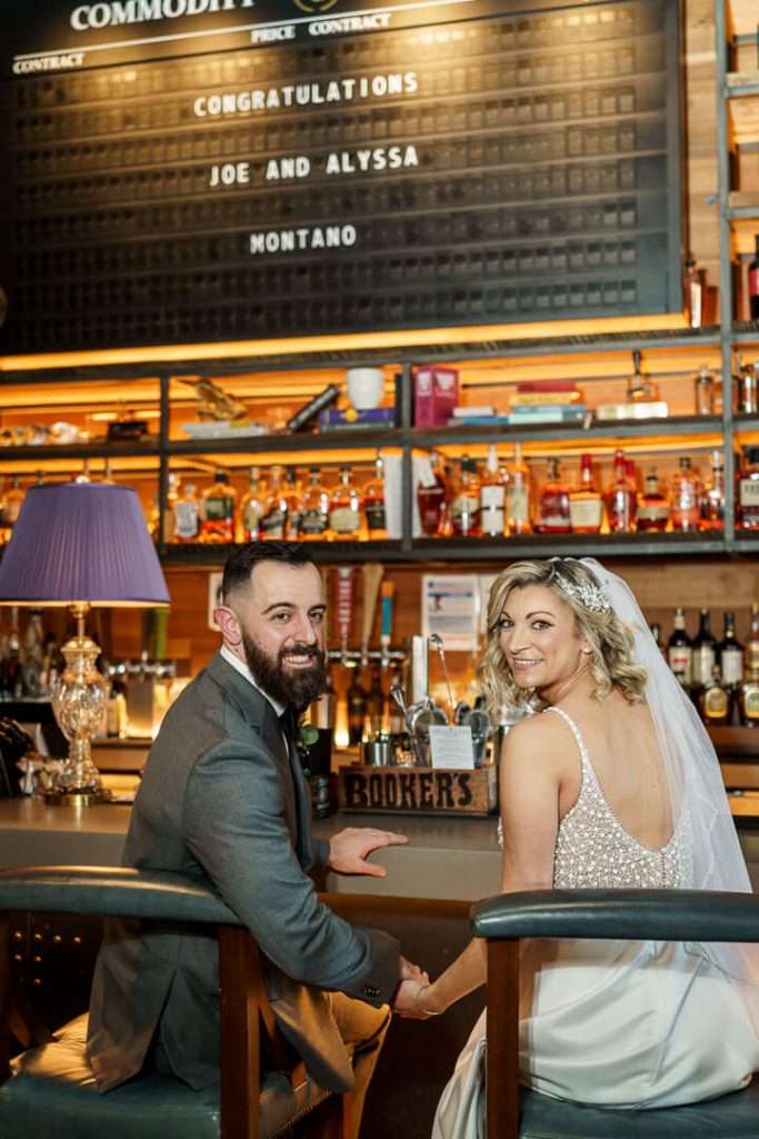Bride and groom holding hands while sitting at the bar, sharing a happy moment at Stone House at Stirling Ridge.