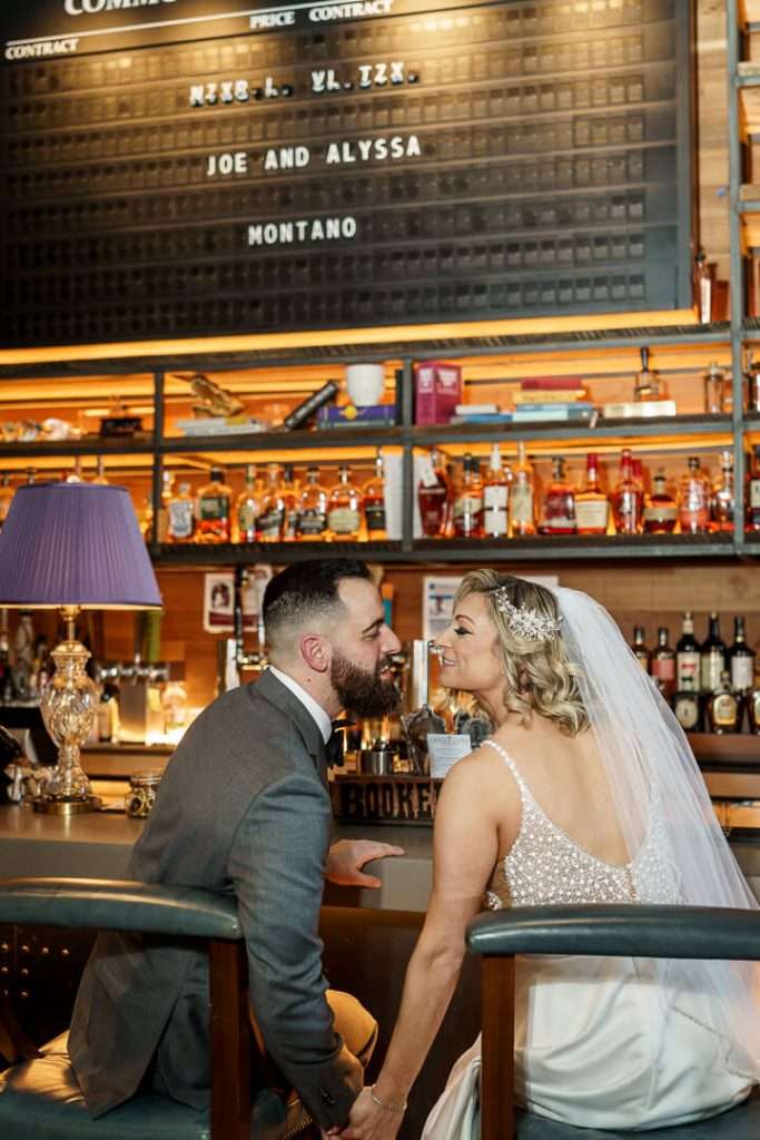 Bride and groom holding hands while sitting at the bar, sharing a happy moment at Stone House at Stirling Ridge.
