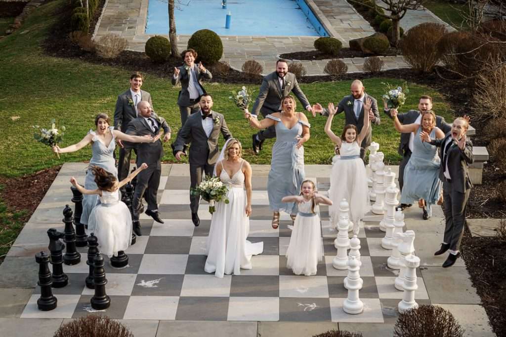 Wedding party jumping in the air in excitement on the outdoor chessboard at Stone House at Stirling Ridge.