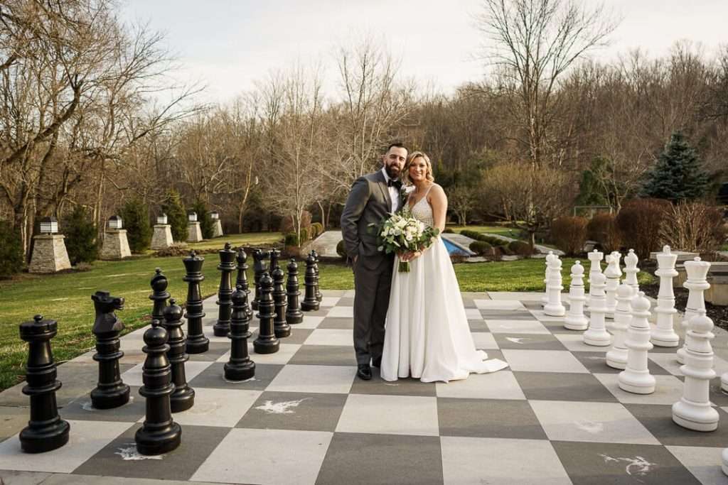 Bride and groom standing together on the life-size chessboard with a scenic nature backdrop at Stone House at Stirling Ridge.