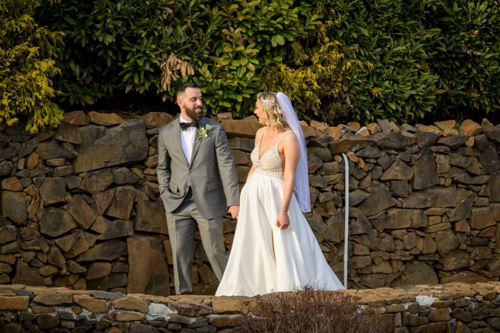 Groom lovingly kissing the bride’s cheek while holding her from behind, outdoors at Stone House at Stirling Ridge.