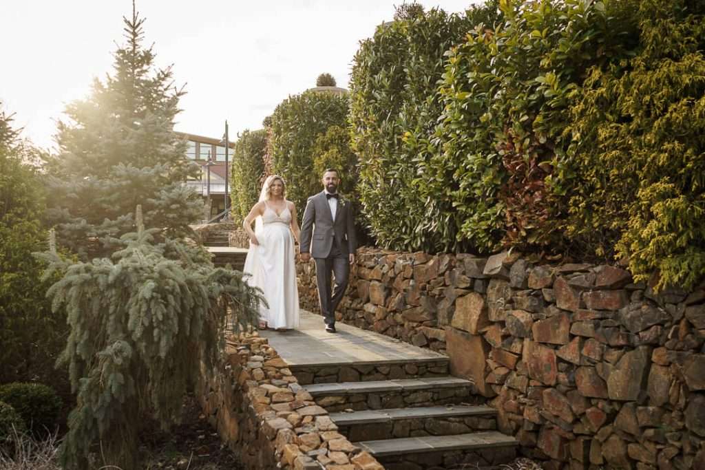 Bride and groom smiling at the camera while standing near a lush green backdrop at Stone House at Stirling Ridge