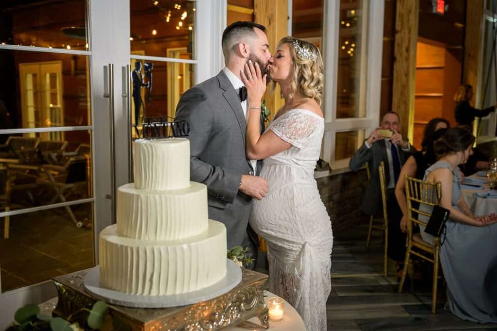 Bride and groom sharing a sweet kiss next to their wedding cake at Stone House at Stirling Ridge