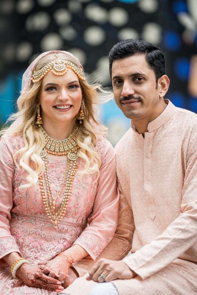 Close-up of smiling couple in South Asian engagement outfits with henna and jewelry