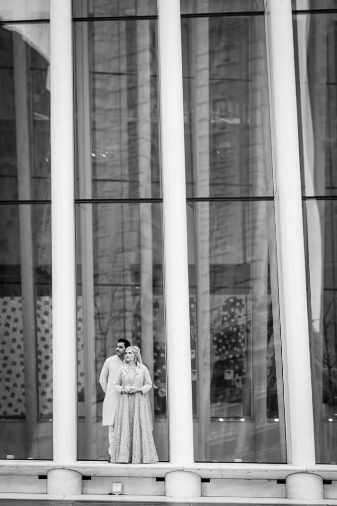 Black and white photo of couple standing in front of reflective glass building structure