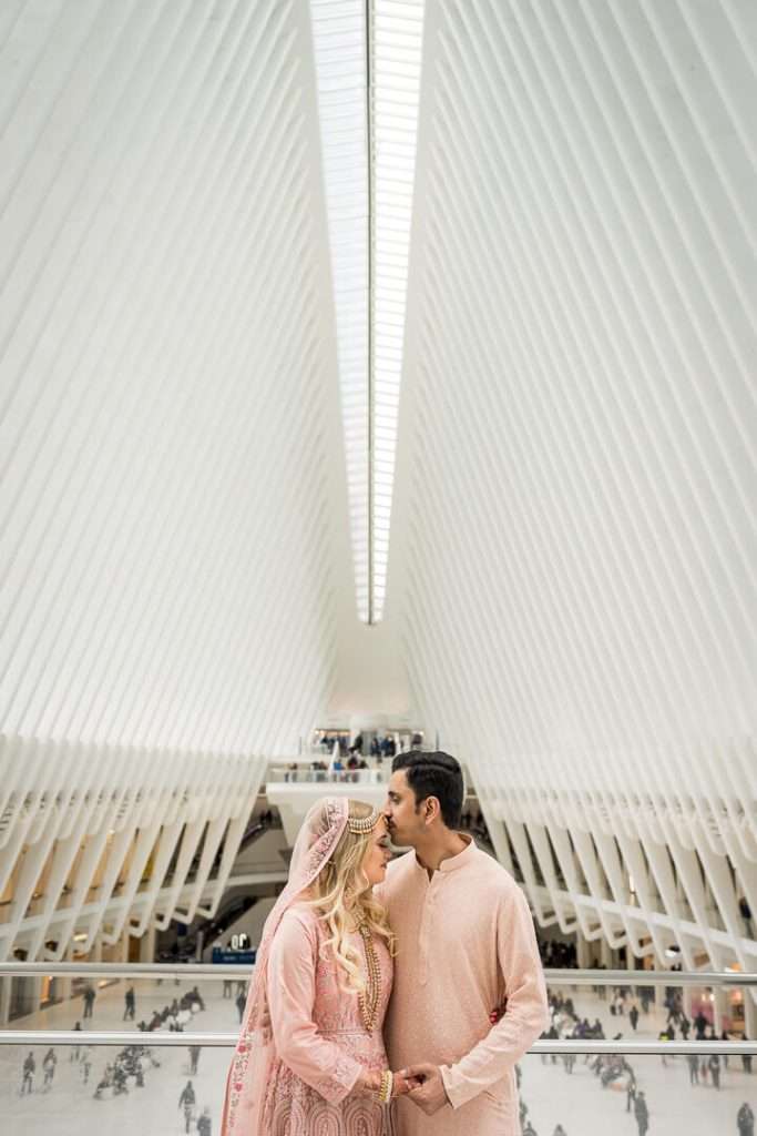 Couple sharing a romantic kiss in traditional South Asian attire inside the Oculus in New York City.