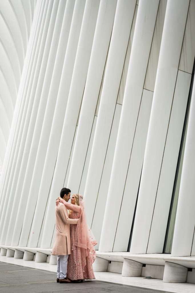 Couple in romantic embrace in front of the vertical white beams of the Oculus building