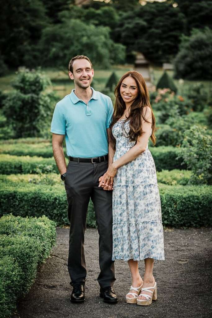Engaged couple posing together in formal garden at Deep Cut Gardens NJ, holding hands and smiling during golden hour portrait session