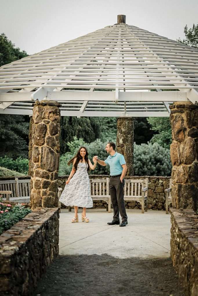 Couple dancing under stone gazebo at Deep Cut Gardens NJ during romantic engagement shoot surrounded by lush greenery