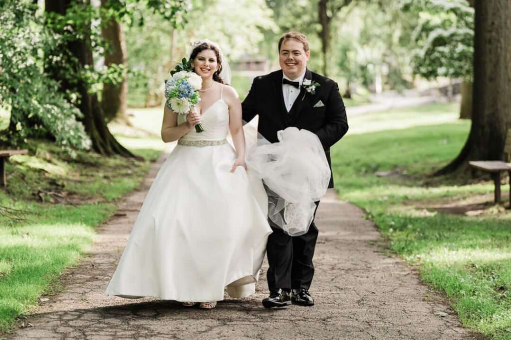 Bride and groom walking down path with bouquet, smiling joyfully during wedding in Nutley, NJ
