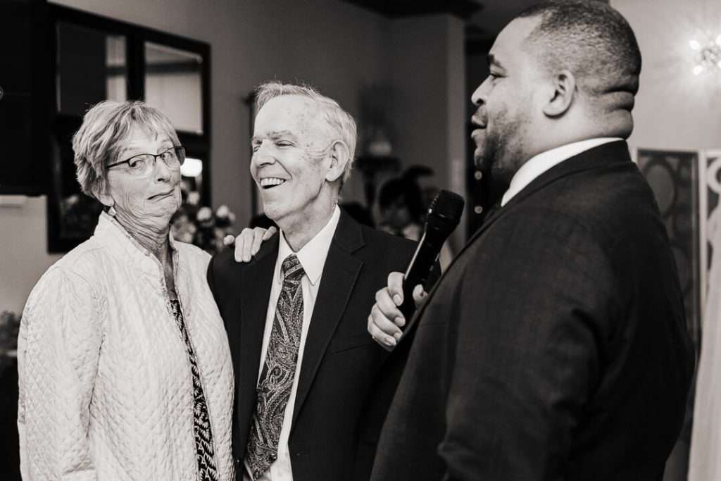 Older couple smiling and laughing with wedding emcee during reception toast at Nutley, NJ venue