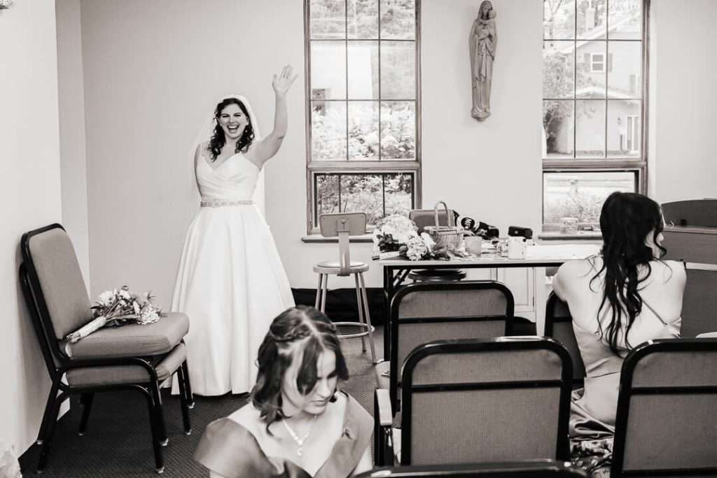Candid moment of bride waving joyfully in the bridal prep room at Our Lady of Good Counsel Church