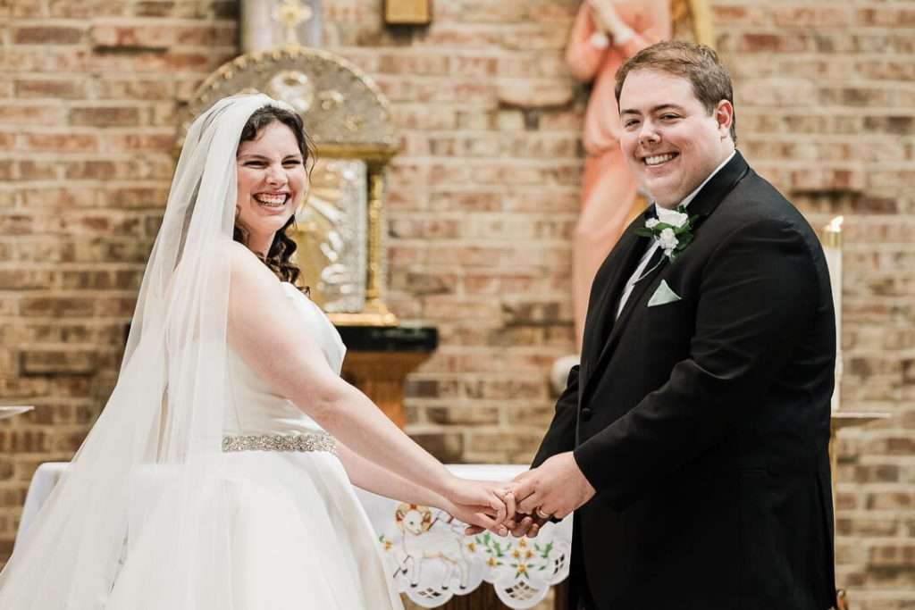Bride and groom smiling while holding hands at the altar during wedding ceremony in Pompton Plains, NJ
